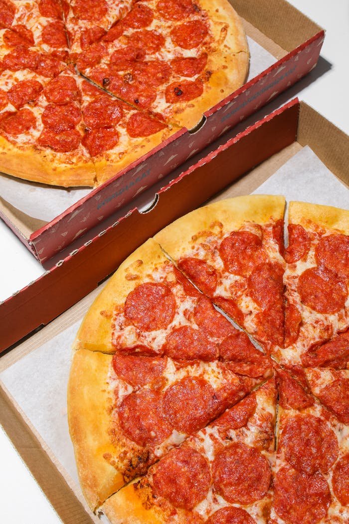 Two pepperoni pizzas in open boxes ready to be served.